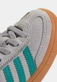 Basket grise en suède avec des rayures zigzag turquoise, tige texturée et semelle en caoutchouc couleur gomme. Présente des lacets gris et des détails de couture.