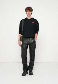 Fekete hosszú ujjú ing, piros "DIESEL" logóval, laza fekete bőr nadrággal, mely zsebekkel van ellátva. A modell egy kis fekete táskát tart.