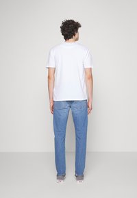 White short-sleeve t-shirt with a relaxed fit, paired with light blue straight-leg jeans. Accessories include gray sneakers.