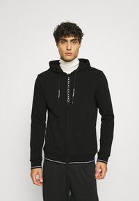 Felpa nera con zip e cappuccio in tessuto morbido, con logo sul davanti. Ha una vestibilità comoda e polsini e orlo a costine.