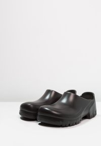 Schwarze Clogs zum Reinschlüpfen mit einer glatten, glänzenden Oberfläche und einer dicken, strukturierten Gummisohle, ausgestattet mit einer abgerundeten Zehenpartie und einem offenen Rücken-Design.