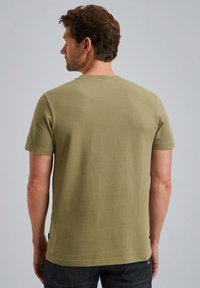 T-shirt vert en coton à manches courtes avec une texture côtelée, col rond et couture visible. La vue arrière montre une coupe droite et une étiquette de logo.