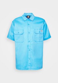 Lichtblauw kortarig overhemd met knopen, gemaakt van een gladde stof. Heeft twee voorzakken en een merkje op de linkerzak.