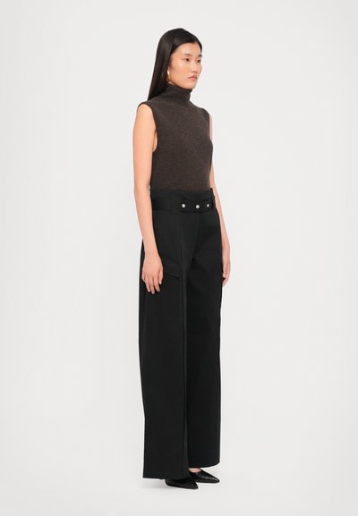 Brown sleeveless turtleneck top paired with high-waisted black wide-leg trousers featuring a belted waist and silver-button accents.
