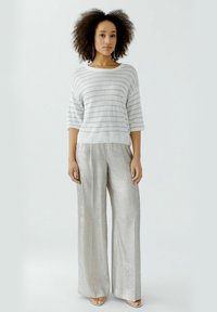 Hellgrauer Strickpullover mit horizontalen Streifen, kombiniert mit silbernen, metallischen weit geschnittenen Hosen. Sanfte Textur und lockere Passform.