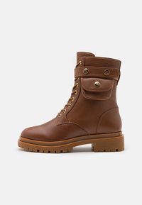 Stivaletti in pelle marrone con suola robusta, occhielli dorati, dettagli con fibbia e tasca laterale. Texture liscia, punta rotonda.