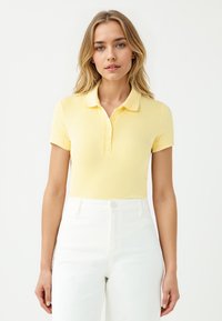 Polo shirt giallo a maniche corte e righe, con colletto classico e bottoni, abbinato a jeans bianchi a vita alta.