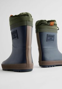Bottes de pluie en caoutchouc avec un corps bleu marine, un bout rond, un dessus olive et une semelle brune. Comprend un patch logo et un cordon de serrage en haut.