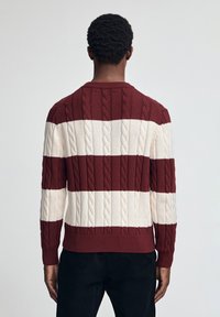 Röd och krämfärgad randig tröja med kabelstickad struktur, ribbade ärmslut och nederkant, med rund halsringning och avslappnad passform.