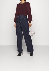 Viininpunainen neulepusero, jossa on teksturoitu kaula-aukko, korkeavyötäröiset tummat farkut ja mustat stiletto-korkokengät. Asusteena hopeinen helmikoristeinen käsilaukku.