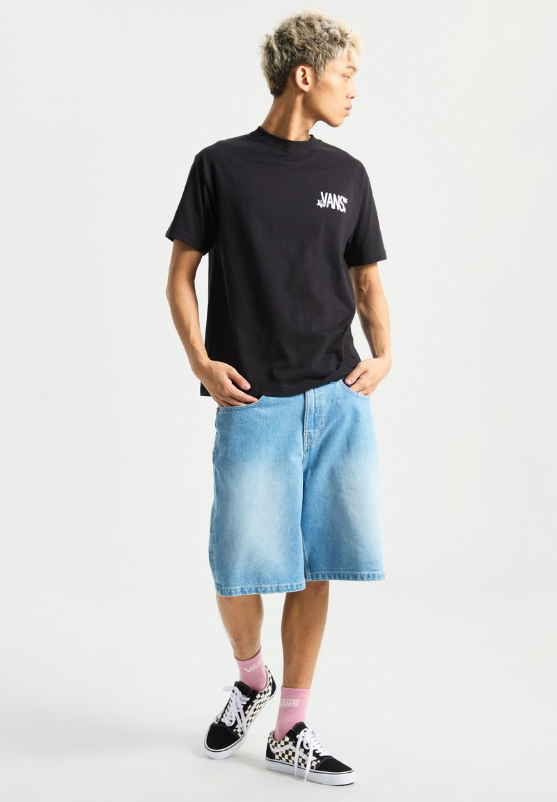 Czarny t-shirt z krótkim rękawem, niebieskie dżinsowe szorty do kolan, różowe skarpetki oraz czarno-białe trampki w szachownicę. Prosty i casualowy styl.