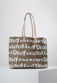 Sac fourre-tout marron avec des poignées beige, orné d'un motif répétant les textes "DKNY", "New York City" et "circa 1989" en blanc sur un fond marqué.
