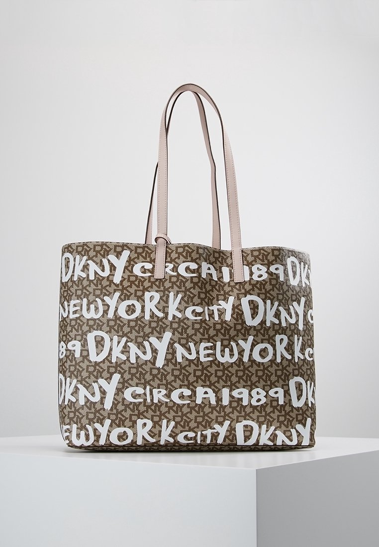 Sac fourre-tout marron avec des poignées beige, orné d'un motif répétant les textes "DKNY", "New York City" et "circa 1989" en blanc sur un fond marqué.