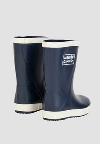 Bottes de pluie en caoutchouc bleu marine avec une bande blanche en haut et une semelle blanche, présentant un logo sur le côté. Texture lisse, hauteur mi-mollet.