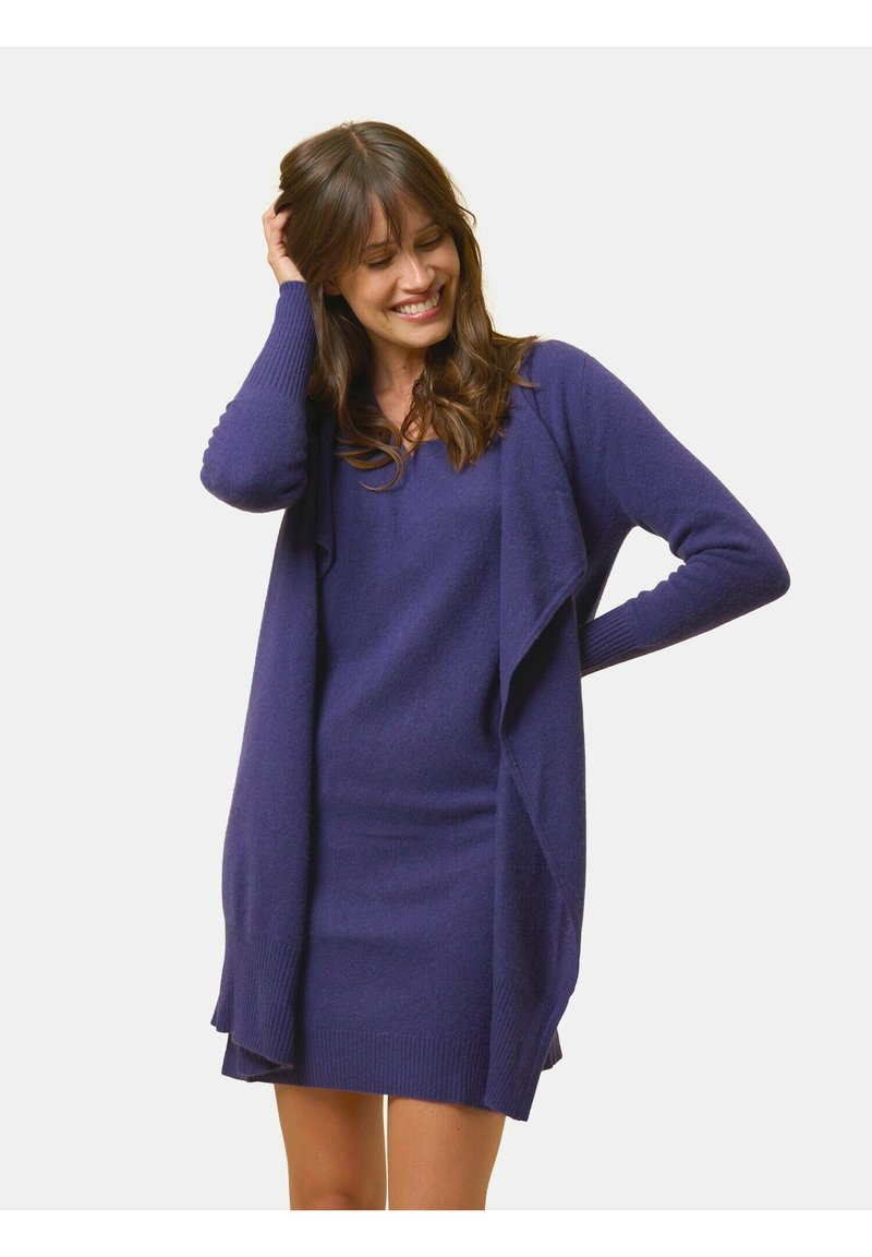 Lila gestrickte Strickjacke mit lockerer Passform, offener Vorderseite, gerippten Bündchen und Saum. Trägt man über einem passenden lila Kleid, weicher Stoff.