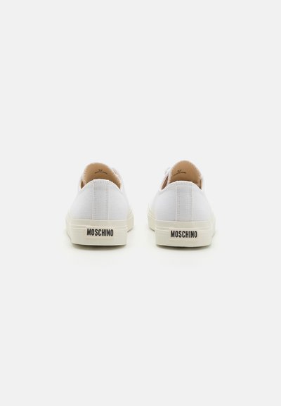 Vita canvas sneakers med rundade tår, beige gummisulor och svart "MOSCHINO"-logotyp på hälen. Enkel, minimalistisk design.