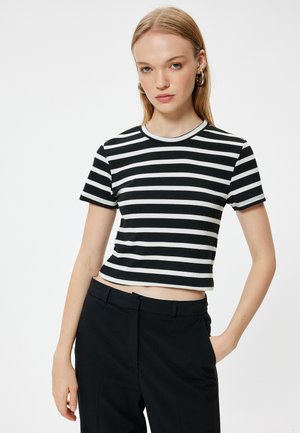 Camiseta corta de rayas blancas y negras con mangas cortas y cuello redondo, hecha de tela acanalada. Combinada con pantalones ajustados negros.