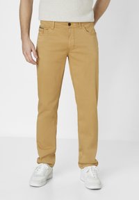 Beige cotton trousers with a straight fit, featuring standard pockets and a button closure. Paired with white sneakers.
