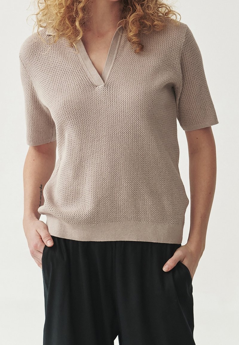 Haut court en maille beige clair à manches courtes, col en V et ourlet côtelé. Présente un motif texturé et une coupe décontractée. Associé à un pantalon foncé.