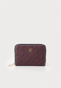 Red and black patterned wallet made of textured fabric, featuring a gold logo and a zip closure, with contrasting stitching accents.