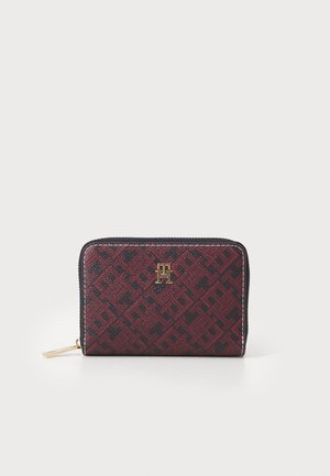 Red and black patterned wallet made of textured fabric, featuring a gold logo and a zip closure, with contrasting stitching accents.