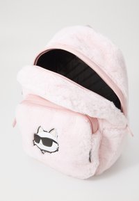 Zaino plush rosa con una texture pelosa, chiusura con zip e design di un gatto cartoon che indossa occhiali da sole sulla parte anteriore. Interno foderato con strisce nere.