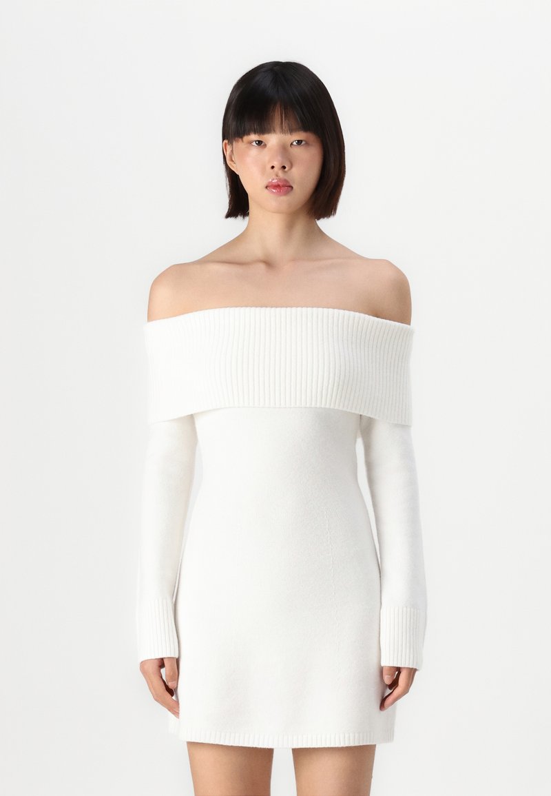 Robe blanche dénudée des épaules avec un col côtelé et des manches longues, fabriquée dans un tissu doux et texturé. Design minimaliste, silhouette ajustée.