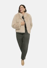 Krótkie, futrzane kurtki w jasnym beżu o puszystej teksturze; noszona na czarną bluzkę, w zestawieniu z szarymi dżinsami i cielistymi szpilkami.