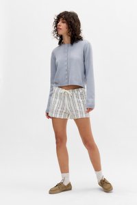 Light blue cropped sweater with button closure, paired with white-striped shorts with a drawstring. Tan shoes and white socks complete the look.