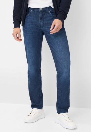 Dunkelblaue Denim-Jeans im geraden Schnitt, mit fünf Taschen, Metallknopf und Reißverschluss, kombiniert mit weißen Sneakers.