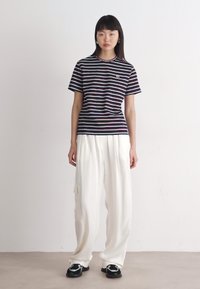 T-shirt à rayures à manches courtes dans des tons marine, blanc et rose, avec un col rond, associé à un pantalon blanc ample et des baskets noires.