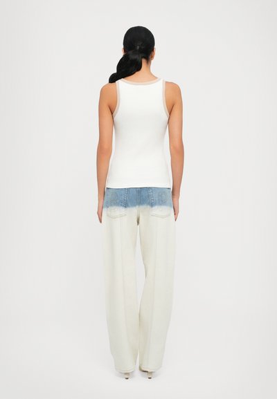 White ribbed tank top with light beige trim, paired with wide-leg light-colored jeans featuring a faded blue waistband and back pockets.
