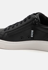 Black leather sneaker with black laces, side zipper featuring "BOSS" pull tab, and white ridged sole.