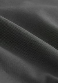 Gros plan sur un tissu gris foncé lisse avec un tissage diagonal fin et des plis doux et fluides créant des ombres délicates.