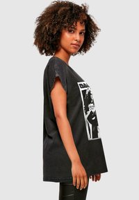 Čierne oversize tričko s netvarovanými rukávmi a grafickou potlačou v bielej farbe. Mäkký bavlnený materiál s voľným strihom.