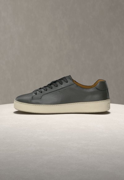 Μαύρο δερμάτινο παπούτσι τύπου sneaker με χαμηλή κορυφή, λευκή λαστιχένια σόλα και μαύρα κορδόνια, τοποθετημένο σε ανοιχτή επιφάνεια με ουδέτερο φόντο.