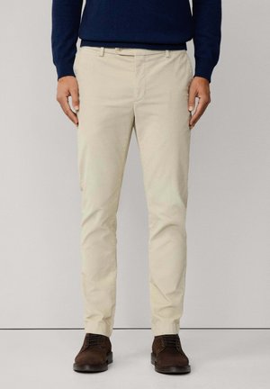 Beige Hosen aus Baumwolle mit geradem Schnitt und subtiler Textur. Kombiniert mit braunen Schuhen und einem marineblauen Pullover.