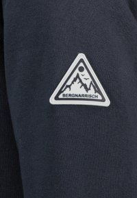 Marineblauwe stof met een zachte textuur heeft een driehoekige witte patch met bergen en de tekst "BERGNARRISCH" in het zwart.