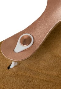 Bruna mockaskor med ett metalliskt roséguldrem, som har en vit knappstängning och mjuk textur, vilket betonar komfort och detaljer.