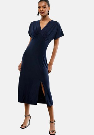 Robe bleu marine, longueur genou, avec des manches courtes, un décolleté en V et une fente sur le côté. Fabriquée en tissu lisse avec des détails plissés au niveau de la poitrine.