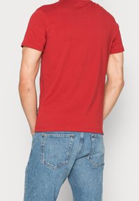 Rød bomulds t-shirt med rund halsudskæring og korte ærmer, sammen med lyseblå denim jeans med baglommer og en afslappet pasform.