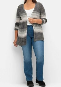 Cárdigan de punto a rayas grises y blancas con abertura frontal, de textura ligera y mangas de tres cuartos, combinado con jeans rectos azules.