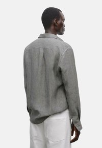 Gray button-up shirt with a subtle texture, back yoke, and a folding collar. Paired with white pants, displaying a casual look.