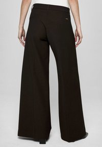 Spodnie o szerokich nogawkach z ciemnobrązowej tkaniny, charakteryzujące się gładką fakturą, tylnymi kieszeniami oraz subtelnym oznaczeniem blisko pasa.