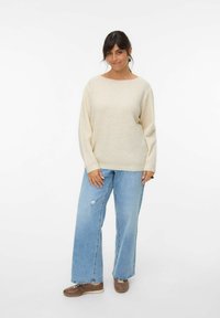 Beige knitted sweater with a loose fit and wide sleeves, paired with light blue distressed wide-leg jeans and brown shoes.