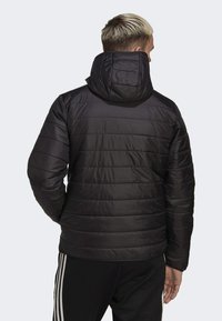 Svart vadderad jacka med huva, med horisontella quiltade linjer, en len textur och framsida med dragkedja. Bärs med träningsbyxor.