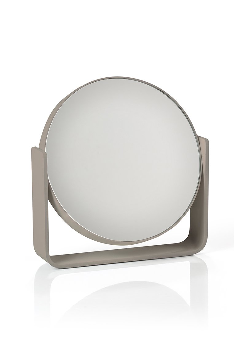 Miroir rond avec une surface réfléchissante lisse, encadré dans un beige mat, soutenu par une base courbée et minimaliste.