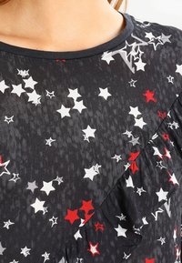 Black fabric top featuring a star pattern in red, white, and gray. Ruffled detail along one side with a round neckline and soft texture.