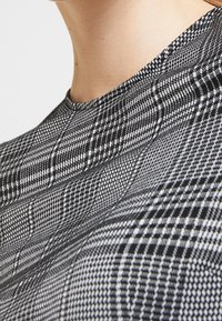 Musta-valkoinen ruudullinen kangas, jossa on teksturoitu kuvio ja vaihtelevan kokoiset ruudut sekä pyöreä pääntie. Lähikuva.