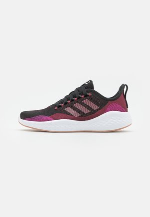 Scarpa da ginnastica atletica nera e rosso scuro con accenti rosa, lacci neri, suola imbottita bianca e linguetta sul tallone, vista laterale.